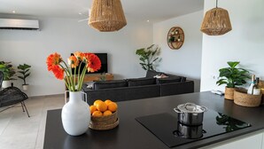 Una cocina moderna con una isla central, encimeras y salpicadero negros. Hay cestas de mimbre con plantas, un jarrón blanco con flores y una botella de vino sobre la isla.