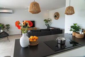 Eine moderne Küche mit Kochinsel, schwarzen Arbeitsplatten und einer schwarzen Spritzschutzwand. Auf der Insel befinden sich Korbwannen mit Pflanzen, eine weiße Vase mit Blumen und eine Weinflasche.