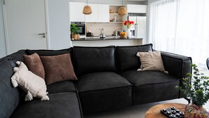 Una sala de estar moderna con un sofá seccional oscuro, una pequeña mesa de centro y vistas a la cocina al fondo.