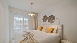 Camera d'albergo con un letto grande, una finestra con tende, un lampadario e due pannelli decorativi a parete.