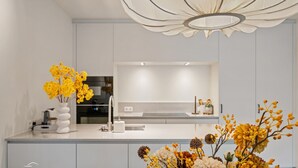 Una cucina moderna con mobili bianchi, un'isola centrale e una lampada decorativa a soffitto.