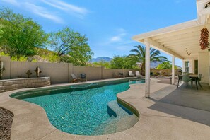 Una piscina con borde curvo, rodeada de sillones de descanso y un área de patio techada.