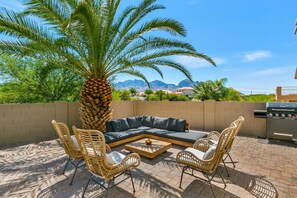 Un patio con un divano componibile, sedie in vimini, un tavolino da caffè, un barbecue e una palma.