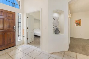 Un corridoio con una porta in legno, una parete bianca con uno scaffale decorativo e un quadro incorniciato.