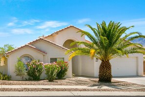 Una casa residenziale con tetto in tegole, una palma e cespugli fioriti.