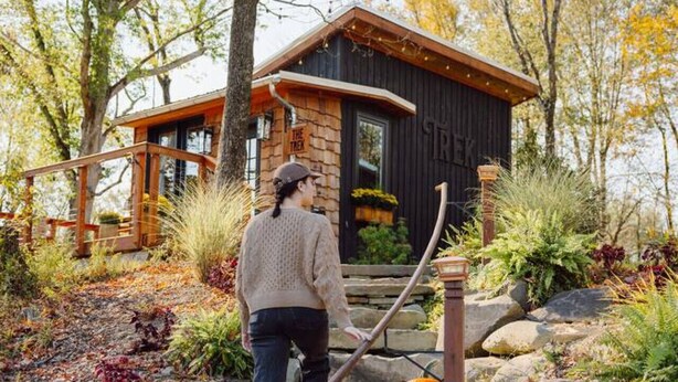 A person ascending a stone staircase with a wooden railing, leading to a cabin with a dark exterior and a wooden deck. - Lux Cabin on Farm, River, Animals, Projector (Montgomery)