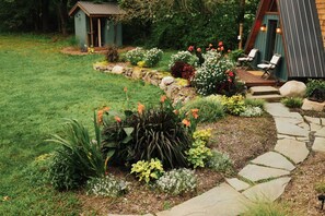 Un jardín cuidado con un sendero de piedra que lleva a una terraza de madera con mobiliario exterior.