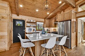 Una cocina moderna con paredes de madera, una isla central, sillas blancas y electrodomésticos de acero inoxidable.