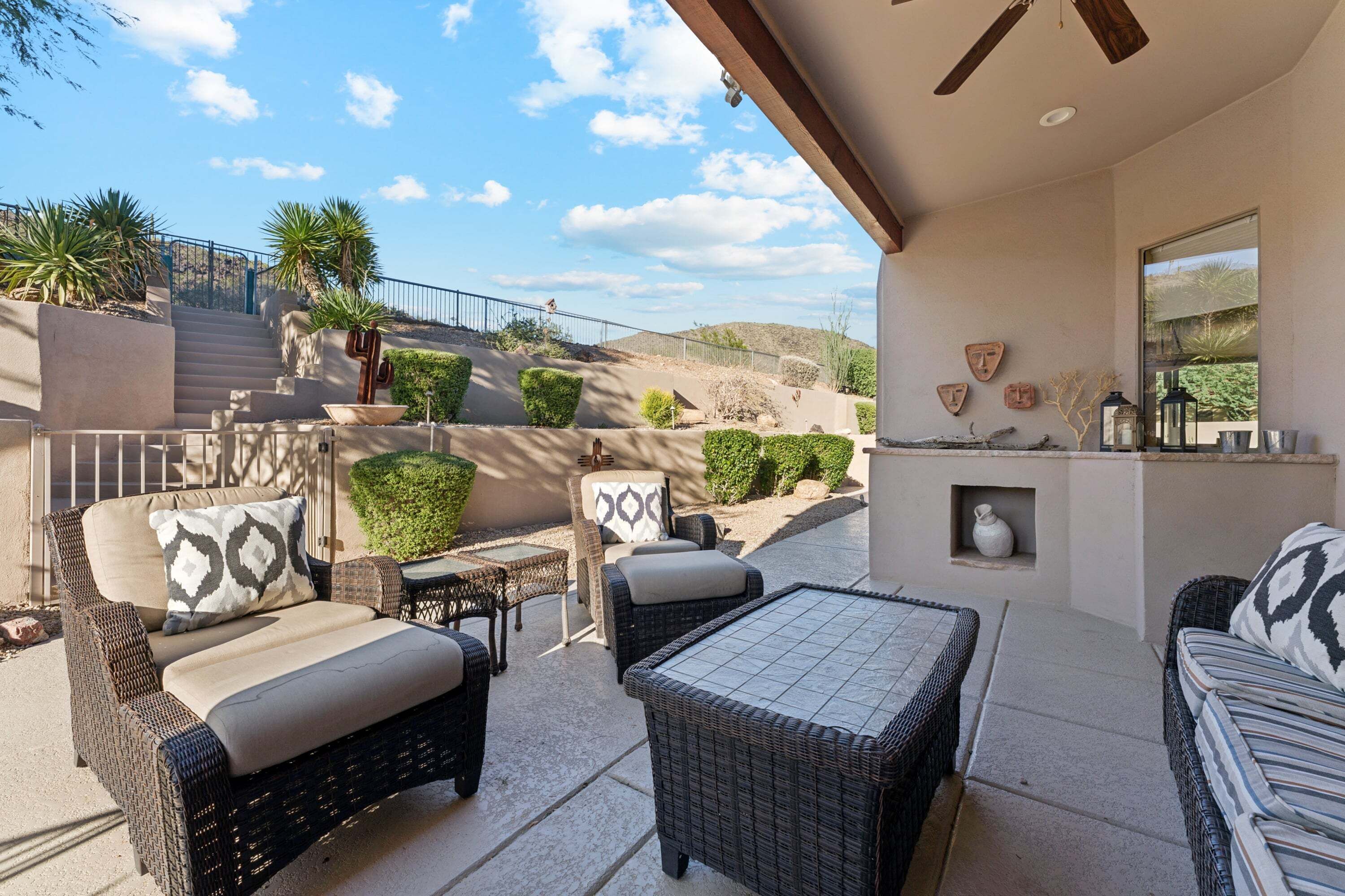 A covered outdoor seating area with wicker furniture, a stone bench, and a view of a hilly landscape.
