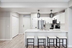 A modern kitchen with white cabinetry, stainless steel appliances, and a central island with bar stools. - Grayhawk Spacious 2 Bedroom Condo/ Community Pool/Fire Pit/Jacuzzi/Fitness (Scottsdale)