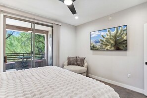 A bedroom with a large bed, a balcony with a table and chairs, and a cactus painting on the wall. - Grayhawk Spacious 2 Bedroom Condo/ Community Pool/Fire Pit/Jacuzzi/Fitness (Scottsdale)