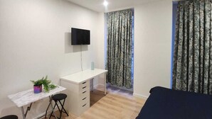 A compact room with a bed, a desk, a chair, a TV, and patterned curtains. - Apparttement distrito10 (Paris)