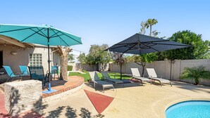Un giardino con piscina, sedie a sdraio e ombrelloni.