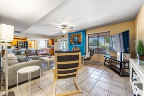 A spacious living room with a sofa, armchairs, a coffee table, and a TV. There is a kitchen area visible in the background. - Quiet Scottsdale retreat with enclosed yard, pool, patio, grill, game room & W/D (Scottsdale)