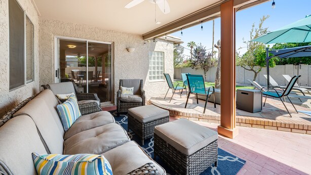 Un'area patio coperta con un divano, poggiapiedi, poltrone in vimini e una ventola a soffitto.