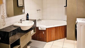 Ein modernes Badezimmer mit einer großen, weißen Badewanne, einer separaten Duschkabine, einem Waschtisch mit Marmorplatte und einem großen Spiegel.