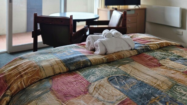 Ein Hotelzimmer mit Bett, Schreibtisch, Stuhl, Fernseher und Blick durch eine Schiebetür.