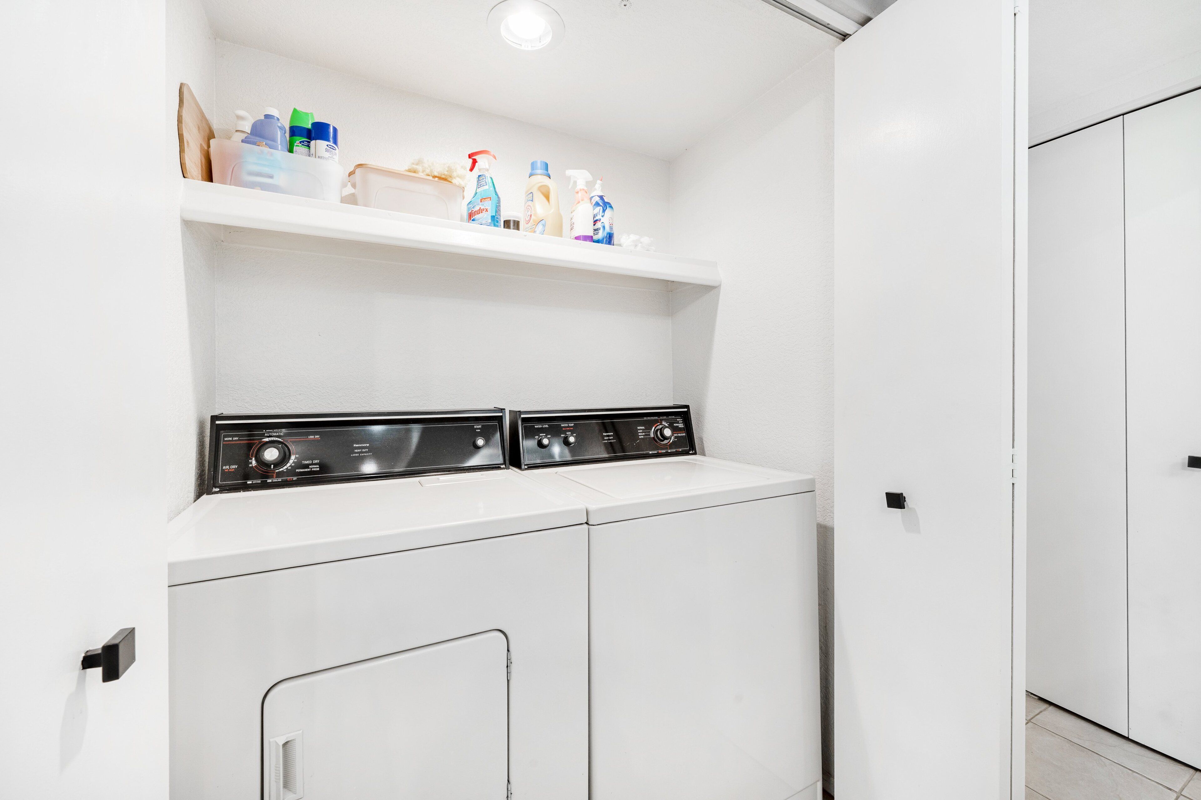 A laundry area with a washing machine and dryer, a shelf with cleaning supplies, and a white door.