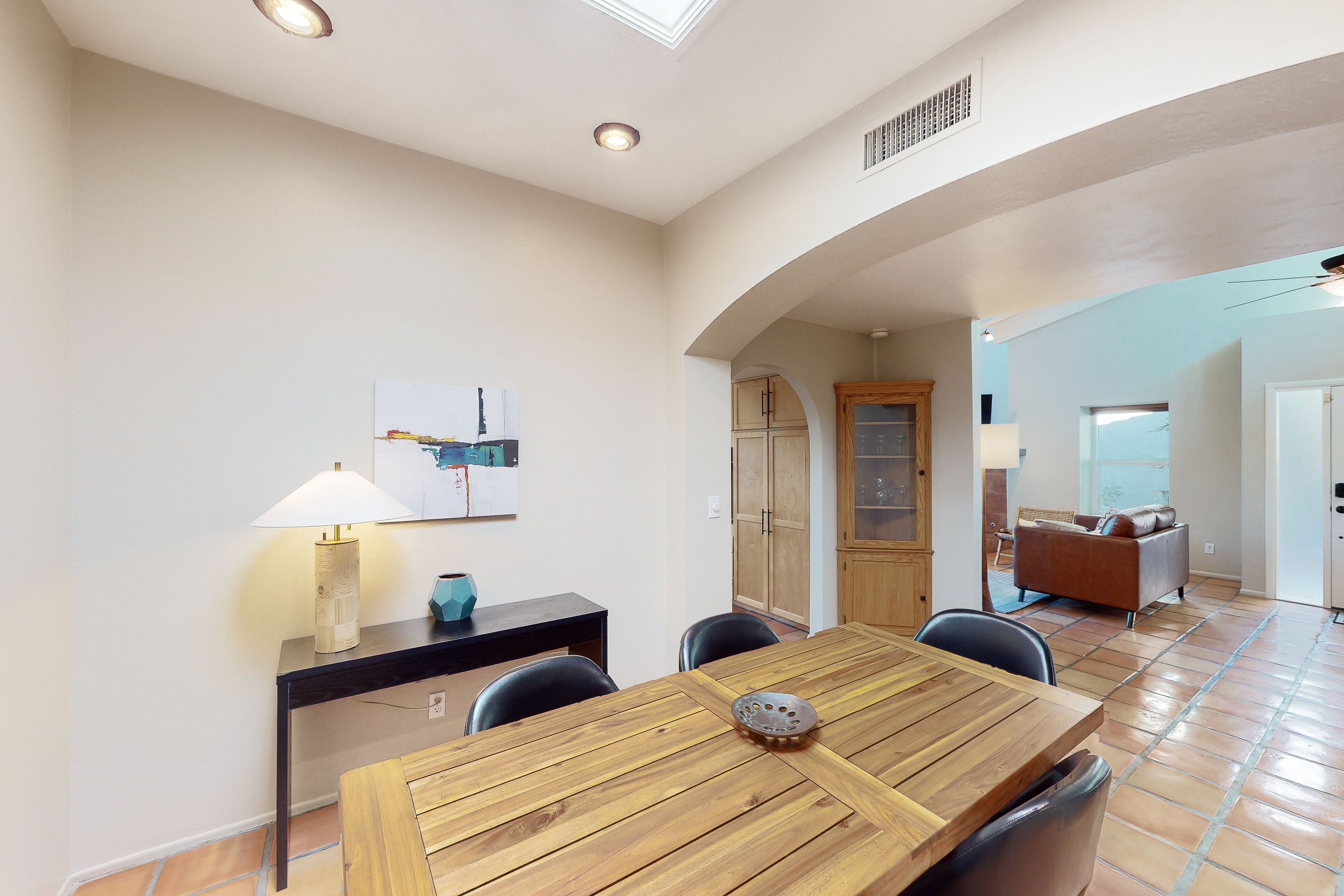 Un comedor con una mesa de madera, sillas, una lámpara y un cuadro en la pared.