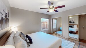 Een slaapkamer met een bed, een plafondventilator, een raam en een schuifdeur naar een badkamer.