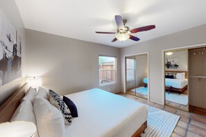 A bedroom with a bed, a ceiling fan, a window, and a sliding door leading to a bathroom. - Stunning Desert Views, Minutes to World-Class Golf & Outdoor Adventures! (Tucson)