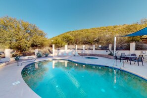 A swimming pool with a curved edge, surrounded by a patio area with chairs and a table. - Stunning Desert Views, Minutes to World-Class Golf & Outdoor Adventures! (Tucson)