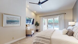 A bedroom with a bed, a ceiling fan, a TV, a chair, a plant, and a window with curtains. - Beautiful single-level home with enclosed yard, pool, patio & WiFi (Scottsdale)