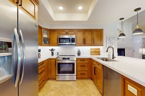 A modern kitchen with stainless steel appliances, wooden cabinets, a large island, and pendant lighting. - Beautiful single-level home with enclosed yard, pool, patio & WiFi (Scottsdale)