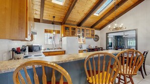 A kitchen with wooden cabinets, a granite countertop, and a dining area with wooden chairs. - Wonderful dog-friendly home with hot tub, firepit, & washer/dryer (Lakeside)