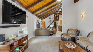 A spacious living room with a high ceiling, a large flat-screen TV, a cozy seating area with leather sofas, and a staircase leading to an upper level. - Wonderful dog-friendly home with hot tub, firepit, & washer/dryer (Lakeside)
