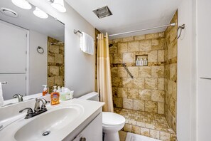 Une salle de bain avec un lavabo blanc, un miroir et des toilettes. On y trouve une douche avec des carreaux de couleur beige et un rideau.