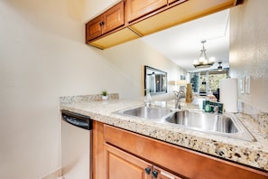 A kitchen with granite countertops, stainless steel sink, wooden cabinets, and a dishwasher. - Stylish Old Town Scottsdale condo with pool, spa, gym, & game room (Scottsdale)