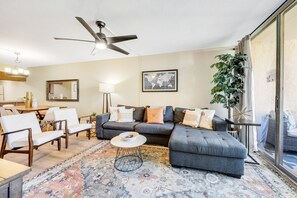 Ein Wohnzimmer mit grauem Ecksofa, weißen Sessel, Couchtisch und einem gemusterten Teppich.