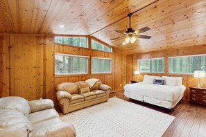A wooden cabin bedroom with a bed, two sofas, a ceiling fan, and large windows. - Spacious home with ping-pong, grill, patio, fast WiFi, & washer/dryer (Pinetop)