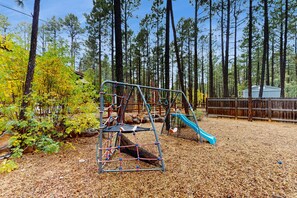 A playground with a rope bridge and slide, surrounded by trees and a wooden fence. - Spacious home with ping-pong, grill, patio, fast WiFi, & washer/dryer (Pinetop)