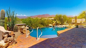 Zona de piscina con vista a montañas, rodeada de cactus y rocas.