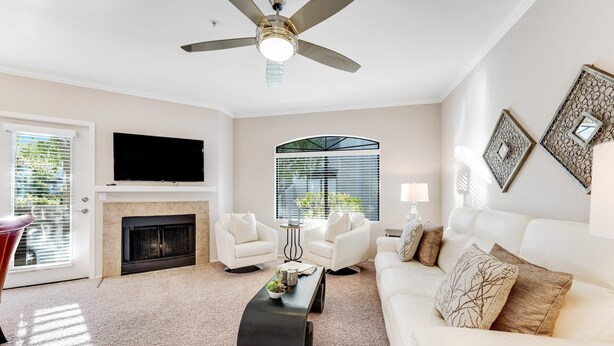 A modern living room with a fireplace, white sofas, a flat-screen TV, and a ceiling fan. - Dog-friendly condo close to the city with central AC, shared pool, & hot tub (Scottsdale)