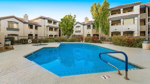 A swimming pool with a blue deck, surrounded by buildings with balconies and a clear sky. - Dog-friendly condo close to the city with central AC, shared pool, & hot tub (Scottsdale)