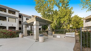 An outdoor patio area with a covered seating area, a barbecue grill, and a trash can. - Dog-friendly condo close to the city with central AC, shared pool, & hot tub (Scottsdale)