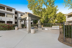 An outdoor patio area with a covered seating area, a barbecue grill, and a trash can. - Dog-friendly condo close to the city with central AC, shared pool, & hot tub (Scottsdale)