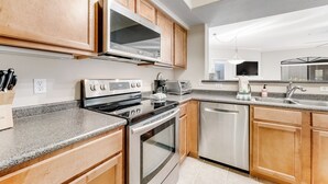 A modern kitchen with wooden cabinets, stainless steel appliances, a granite countertop, and a dishwasher. - Dog-friendly condo close to the city with central AC, shared pool, & hot tub (Scottsdale)