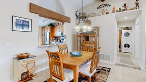 Un comedor con una mesa y sillas de madera, una araña y una cocina al fondo.