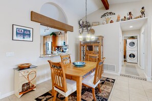 Un comedor con una mesa y sillas de madera, una araña y una cocina al fondo.