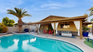 A swimming pool with a covered patio area, red chairs, and a palm tree. - Charming, dog-friendly home only minutes to Old Town with pool & custom bar (Scottsdale)