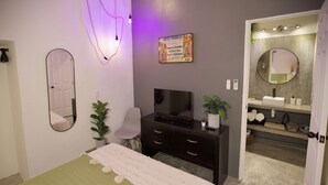 Une chambre à coucher comprenant un lit, une télévision, un miroir, une commode et une salle de bain avec un lavabo et un miroir.