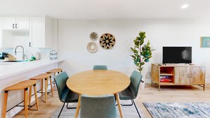 A modern kitchen with white cabinets, a wooden dining table with four chairs, a TV on a wooden cabinet, and decorative wall art. - 2-story dog-friendly condo with patio, outdoor pool, W/D, streaming, partial AC (Scottsdale)