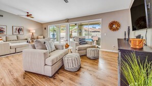 A spacious living room with a large sofa set, ottomans, and a coffee table. There are ceiling fans, a fireplace, and a view of a pool and house through large windows. - Desert stay with a private pool, grill, washer/dryer, & central AC (Glendale)