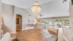 A spacious living room with a round wooden table, beige sofas, a chandelier, and a view of a swimming pool. - Desert stay with a private pool, grill, washer/dryer, & central AC (Glendale)