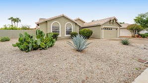 A single-story house with a beige exterior, a garage, and a gravel driveway. - Desert stay with a private pool, grill, washer/dryer, & central AC (Glendale)