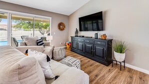 A living room with a sofa, ottoman, and a TV mounted on the wall. - Desert stay with a private pool, grill, washer/dryer, & central AC (Glendale)